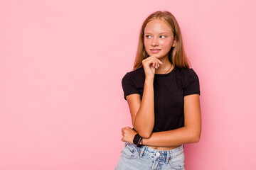 Caucasian teen girl isolated on pink background looking sideways with doubtful and skeptical expression.