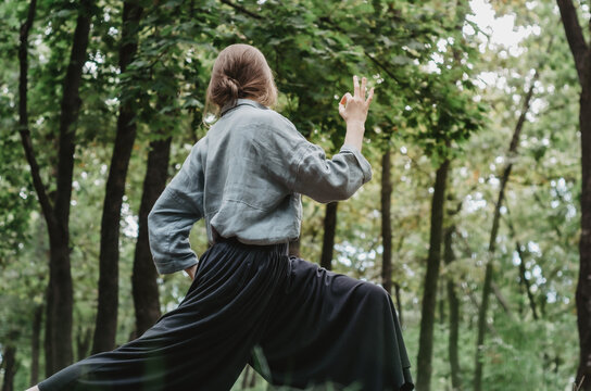 Woman in loose, comfortable clothes doing yoga in the forest, showing ok sign
