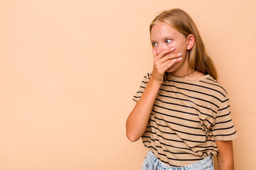 Caucasian teen girl isolated on beige background thoughtful looking to a copy space covering mouth...