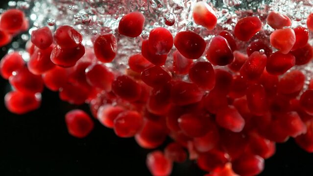 Super slow motion of falling pomegranate pieces into water. Isolated on black background. Filmed on high speed cinema camera, 1000fps