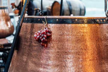 Bunch of grapes hanging on the pot of mulled wine in a stall in a Christmas market. Close Up of mulled wine in traditional copper cauldron. Seasonal concept. Selective focus. - obrazy, fototapety, plakaty