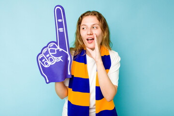 Young caucasian sports fan woman isolated on blue background is saying a secret hot braking news and looking aside