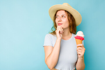 Young caucasian woman holding an ice cream isolated a blue background looking sideways with...