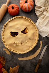 Cooking halloween apple pie, pumpkin face cutted in raw dough. Autumn baking concept, top view.