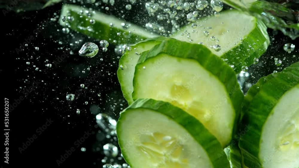 Aufkleber Super slow motion of falling cucumber slices into water. Isolated on black background. Filmed on high speed cinema camera, 1000fps. Speed ramp effect.