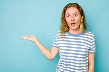 Fototapeta premium Young caucasian woman isolated on blue background impressed holding copy space on palm.