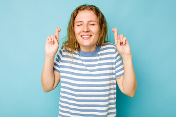 Young caucasian woman isolated on blue background crossing fingers for having luck