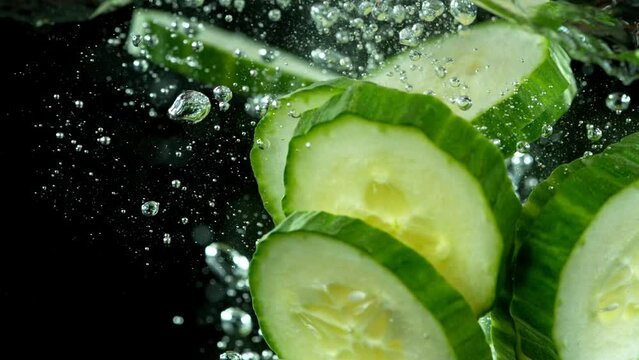 Super slow motion of falling cucumber slices into water. Isolated on black background. Filmed on high speed cinema camera, 1000fps. Speed ramp effect.