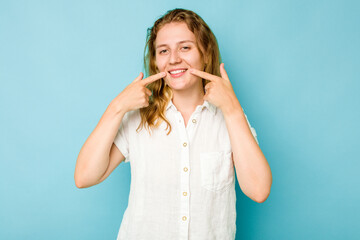 Young caucasian woman isolated on blue background smiles, pointing fingers at mouth.