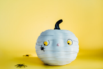 Funny and cute pumpkin mummy with spider on the yellow background. White Pumpkin with scaried and...