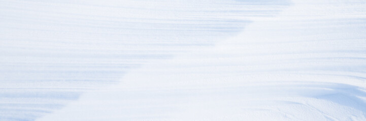 Beautiful winter background with snowy ground. Natural snow texture. Wind sculpted patterns on snow surface. Wide panoramic texture for background and design.