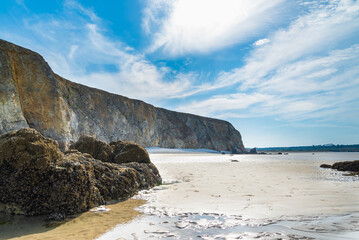 The famous beach of Kersiguenou, Brittany, France, during low tide. Black rocks in the foreground. Cliffs with blue sky and clouds on the background.