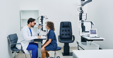 Pediatric ophthalmology. Optometrist checking eyesight of boy patient at modern eye clinic - obrazy, fototapety, plakaty