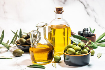 Olive oil in two glass containers and harvest olives berries in bowls on a light background.