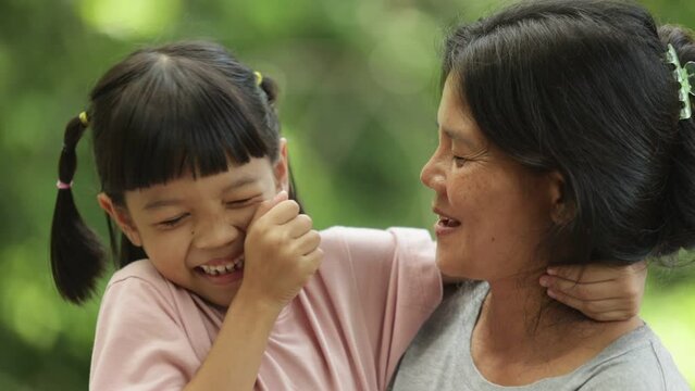 Portrait of a Thai mother and daughter of Asian descent are sitting in the outdoor park happily and cheerfully smiling face Be a loving mother a warm family The background is green trees.