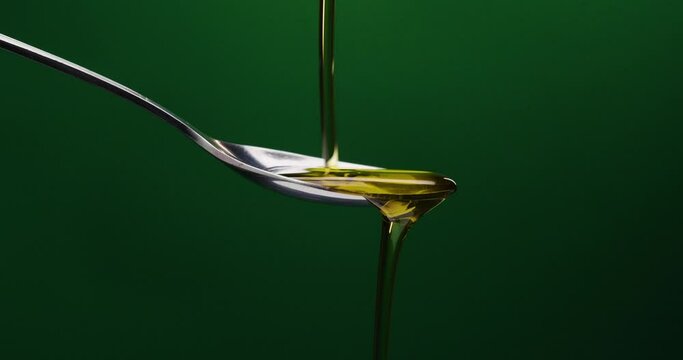 Static shot of spoon over which oil is poured against green background