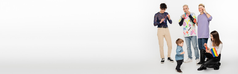 toddler boy near young lgbtq community friends blowing soap bubbles on grey background, banner.