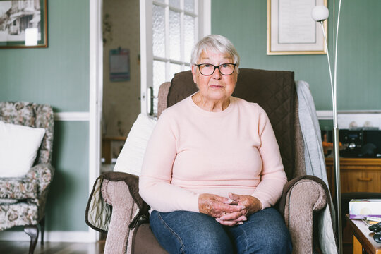 Portrait of smiling senior, mature retired grandmother in eyeglasses, elderly woman smiling, sitting on the armchair at home enjoying retirement. Selective focus.