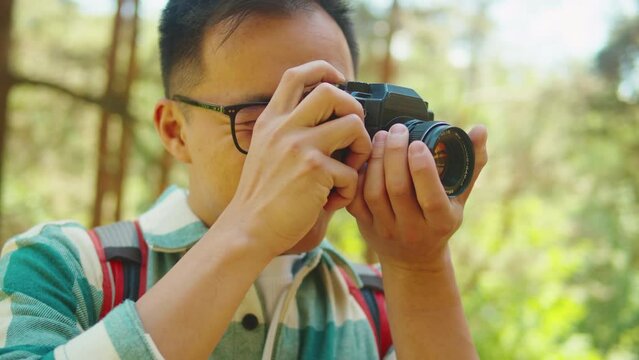 Asian man taking photo in forest, tourist photographer using camera , safe travel and explore, walking hiking tours. Traveling and hiking alone. Summer tourism, wild nature. 