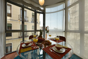 Circular glass dining table with fresh fruit and orange juice with a large glass bay window