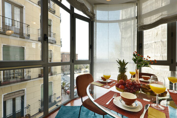 Circular glass dining table with a nice and healthy breakfast with fresh fruit and orange juice with a large glass window overlooking the city