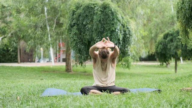 Man stretching body while sitting on a yoga mat outdoors in a park.