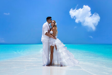 Fototapeta na wymiar Summer love. Beautiful happy young couple in wedding clothes is standing on a beach in the Maldives. Engagements and wedding on the beach on the paradise island of Maldives. Luxury travel.