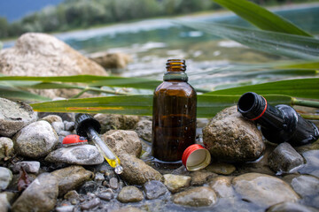Plastik Flasche mit Mettal Deckel und Pipette mit Öl drinnen im See,Laub,Steine ,auf eine ist Marienkäfer