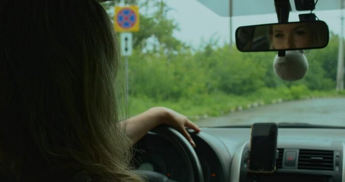 A woman holds the steering wheel of a car with one hand, adjusts the mirror in a Toyota Corolla sedan with the other, sits in a chair and is ready to go before starting a trip