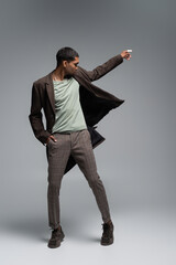 full length of young african american man in autumnal woolen coat posing with hand in pocket on grey.