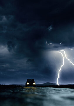 Vintage pickup truck with illuminated headlights on road in vast landscape under a dark sky with lightning. 3D render.