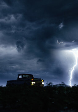 Vintage pickup truck with illuminated headlights in countryside under a dark sky with lightning. 3D render.
