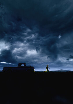 Man runs away from a vintage pickup truck with illuminated headlights in countryside under a dark sky. 3D render.