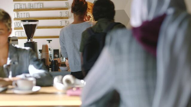 Cafe, coffee shop and barista serving a customer while standing behind a bar counter. Friendly service of a female worker, staff or waiter in apron while helping people or taking order in coffeehouse