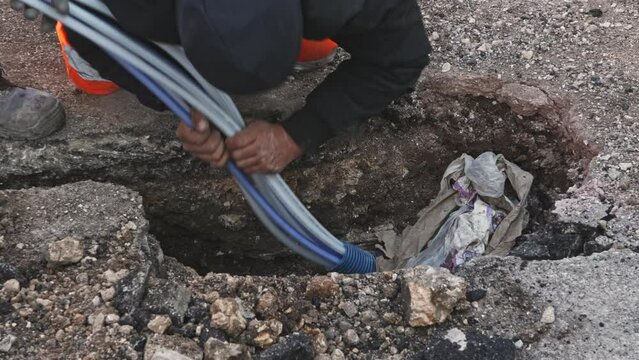 Worker slips fiber optic cables into underground corrugated pipe