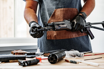 Close up of young man in apron disassembling a gun above the table