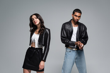 young interracial couple in black leather jackets looking at camera isolated on grey.