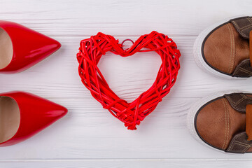 Red knitted heart and footwear on white desk. Red female shoes and male shoes.