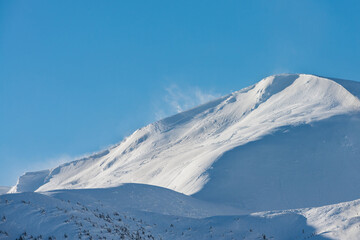 Fototapeta na wymiar Snow-covered mountain top. The wind rises the snow on the mountain range.