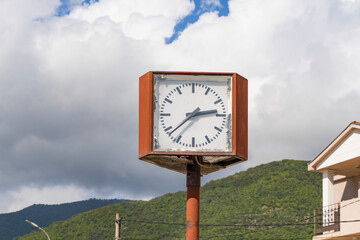 an old square street clock rusted with time. Street dial. A clock on a pole in a large city.