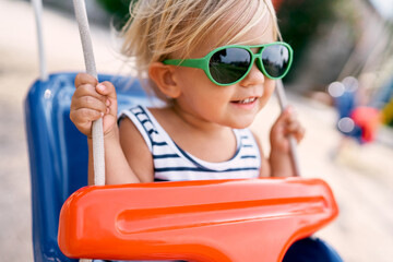 Little smiling girl in sunglasses on a swing. High quality photo