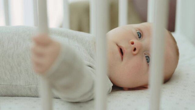 Close up of plumpy infant kid dressed in baby grow lie on plaid in baby cot look around explore world. Newborn baby concept