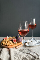Rose wine with ripe figs, camembert cheese and cashews on a table indoors.