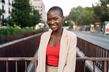 Smiling african american young woman standing and looking at camera on a footbridge in the city