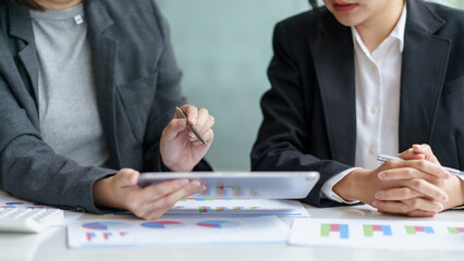 Two business people are using a tablet to present their work at a meeting showing their income, financial statements, balance sheets, taxes, quarterly, yearly.
