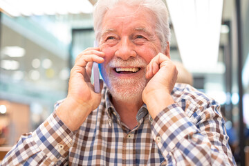 Happy smiling senior bearded man sitting inside a cafeteria talking on mobile phone - caucasian beautiful elderly male enjoying technology