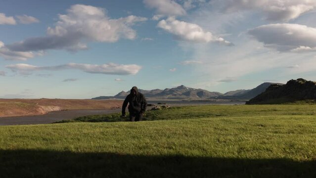 Man in black outdoors clothes walking towards camera on green grass in rural Iceland.