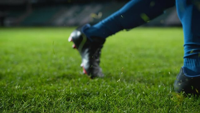 Close-up of a Leg in a Boot Kicking Football Ball. Professional Soccer Player Hits Ball with Fierce Power, Scores Goal, Grass Flying. Super Slow Motion Cinematic Low Angle Ground Artistic Shot