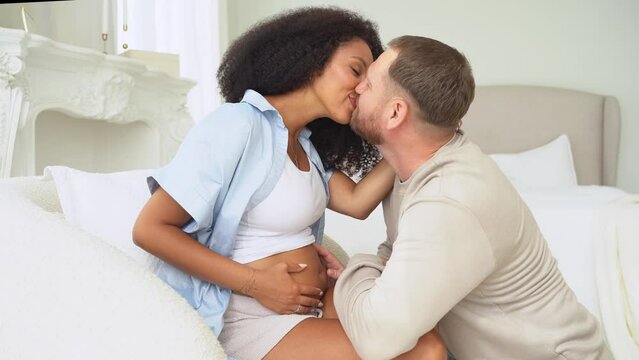 White man touching belly of his pregnant black wife. Pregnancy and loving husband hugging tummy at home. Feeling baby movement by multiethnic couple in pregnant belly.