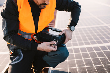 Cropped picture of worker opening toolbox while crouching on the rooftop covered with solar panels.
